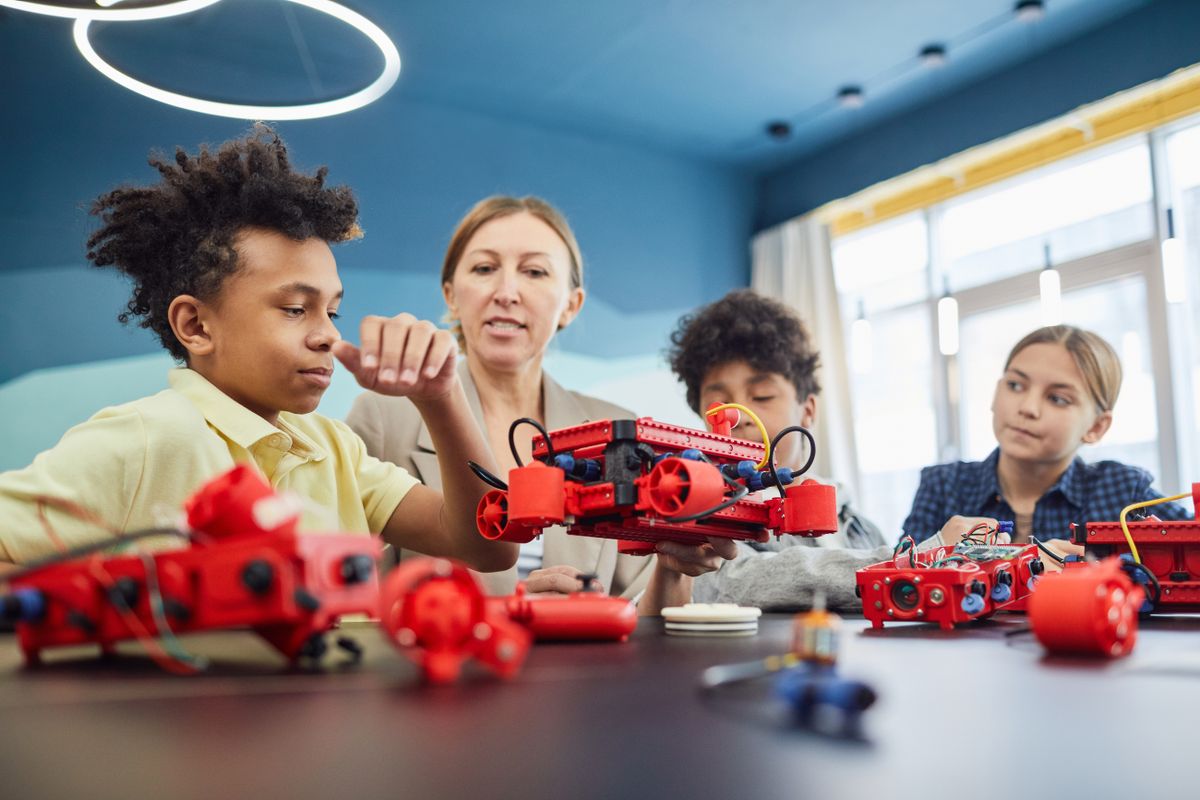 Students assembling robot kits at a table with an instructor guiding them